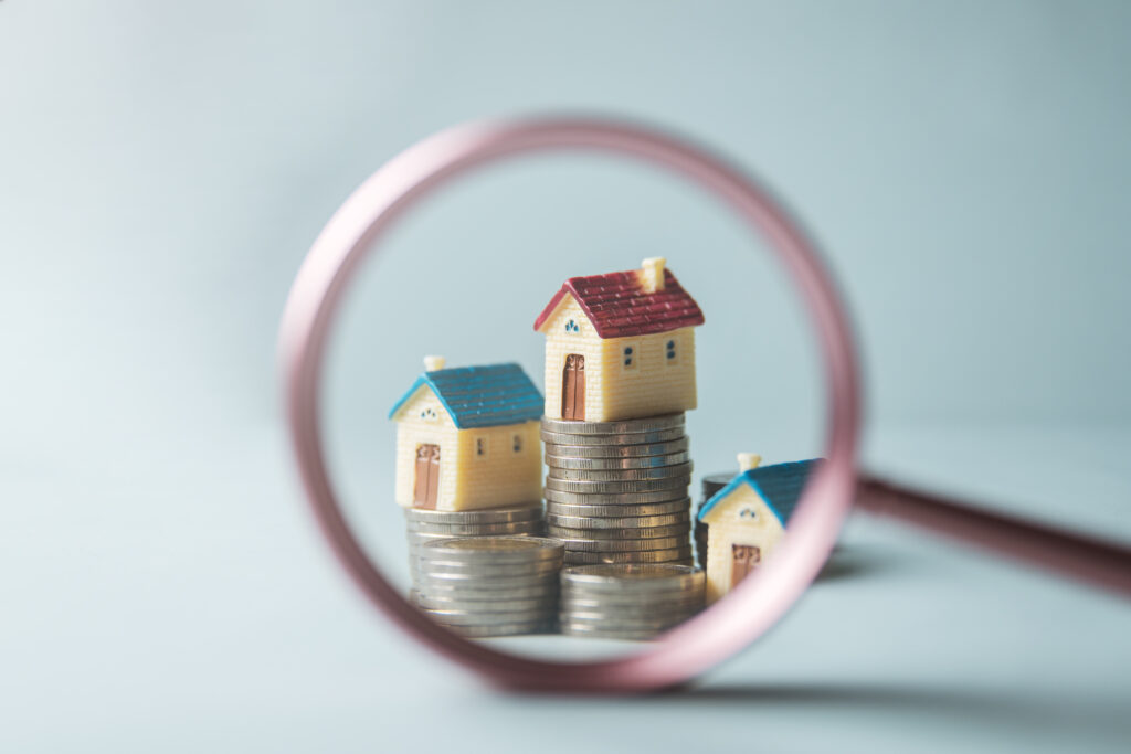 Real estate invest growth. Real estate asset property. Mortgage residential finance. A magnified view of three small houses stacked on top of each other with coins on top of the houses.